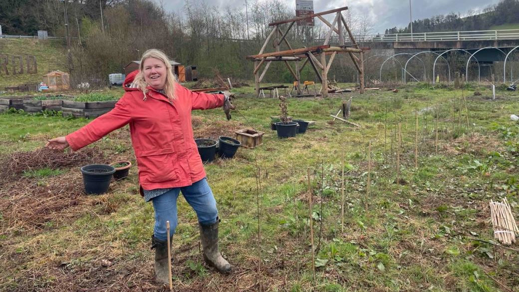 A volunteer gardener in a red jacket in the garden, welcoming you with open arms